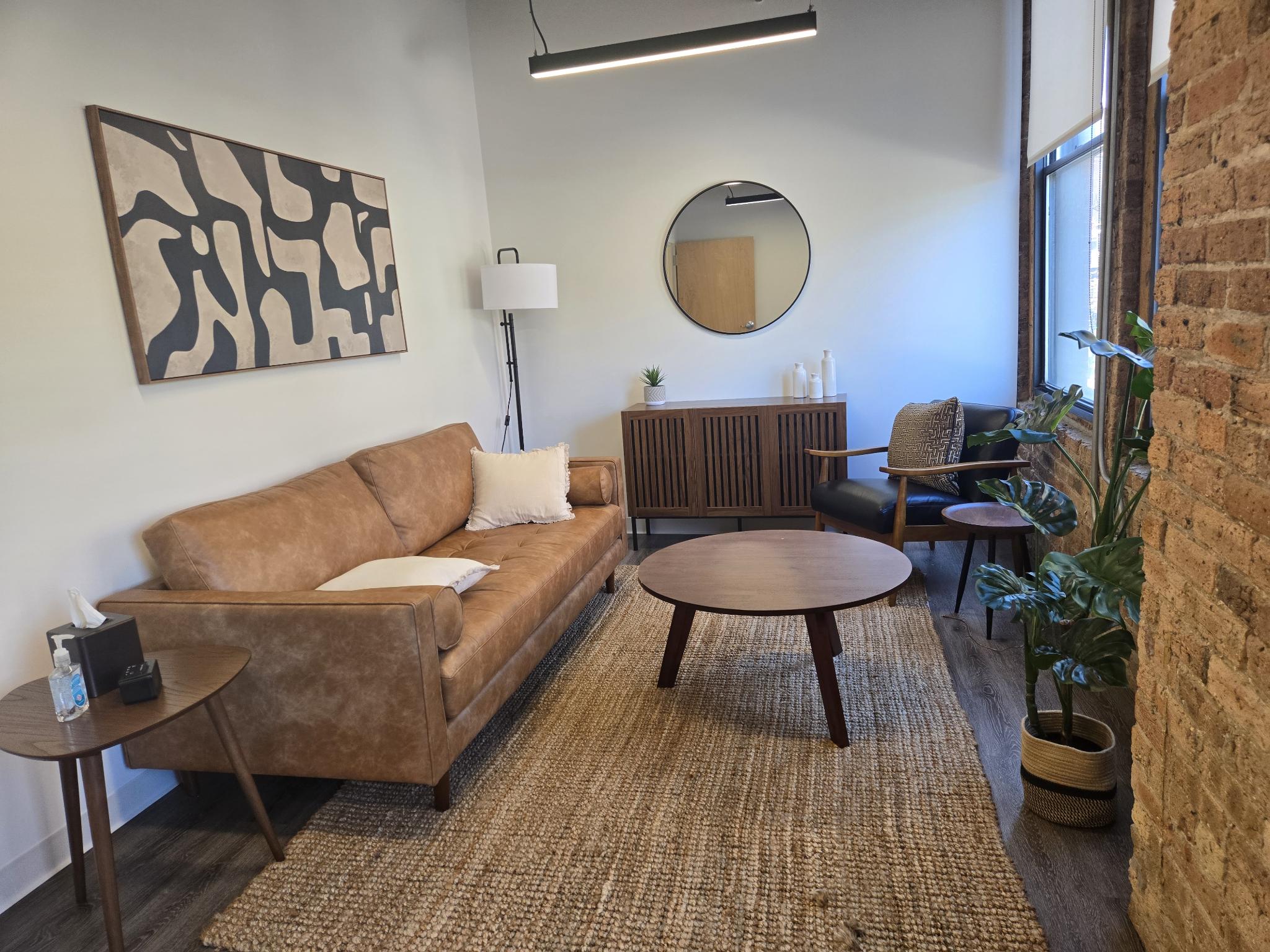 A warm therapy office with a leather sofa, chair, and soft natural light